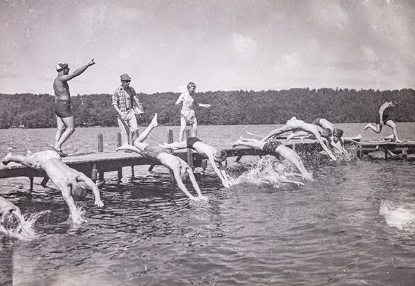 A group of boys diving into a lake from a wooden dock