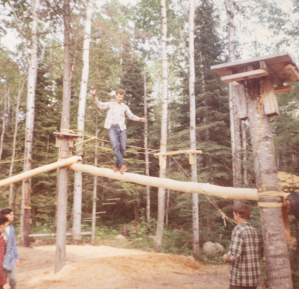 A person balances on a log suspended between trees in a forest