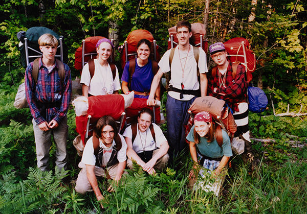 A group of hikers with large backpacks smiles in a forest
