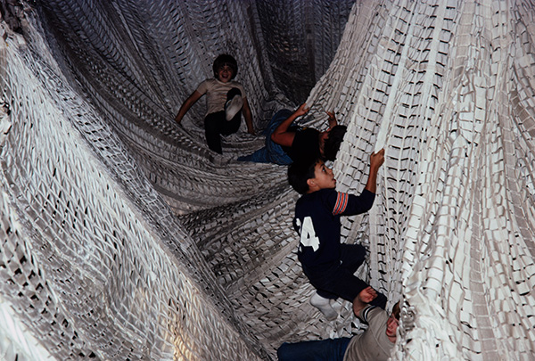 Children climb through a network of large, suspended white nets indoor