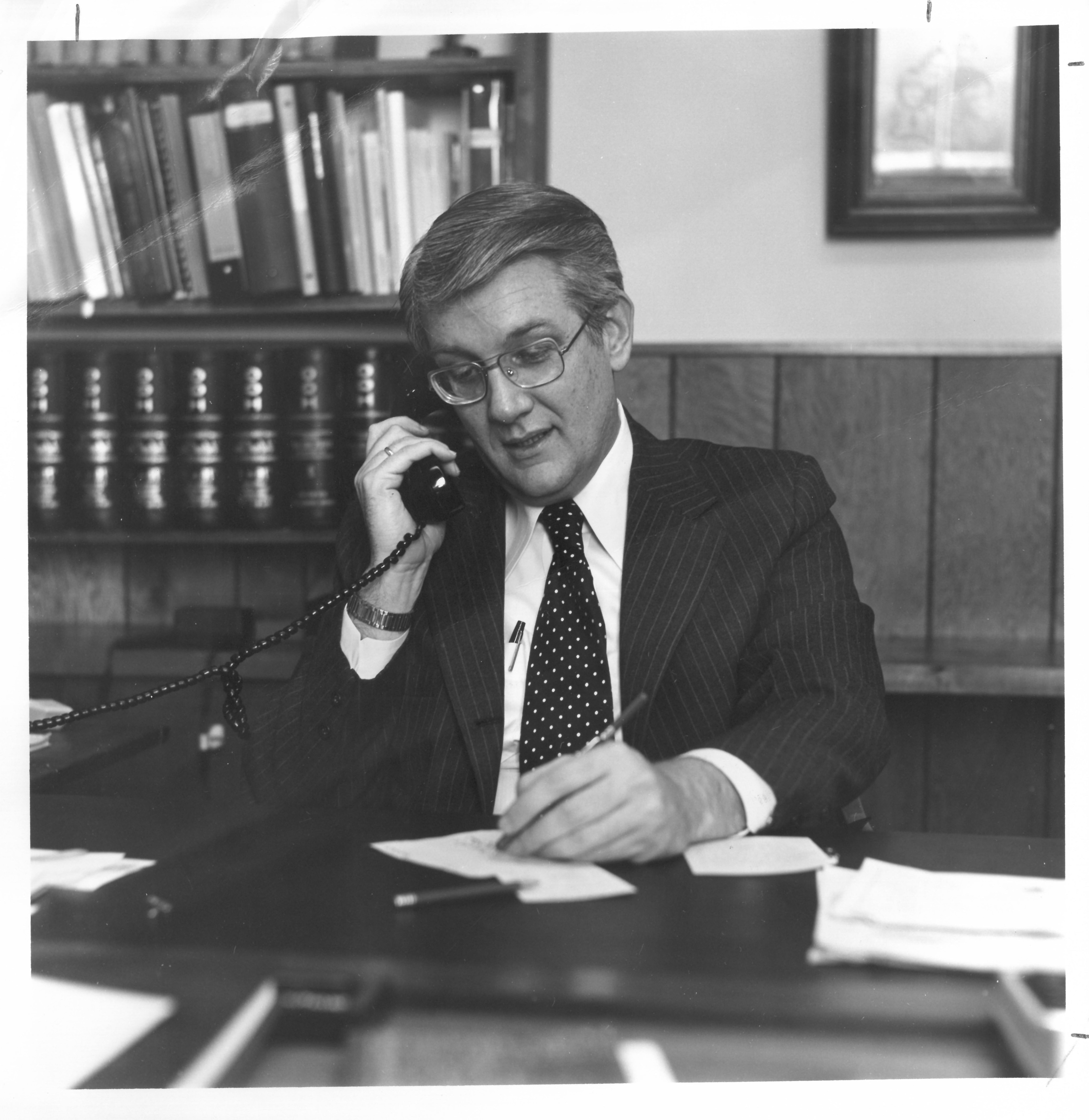 Dr. Bill Pollard wearing a suit and taking notes while on the phone in his office