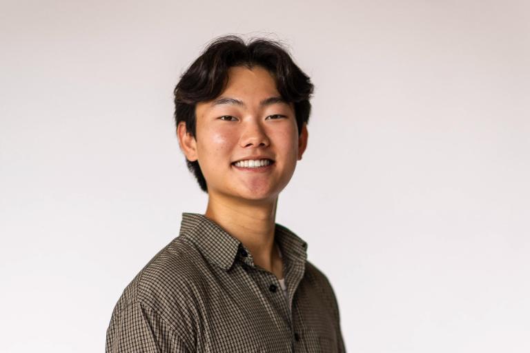 Student wearing button down shirt stands smiling with hand in pocket