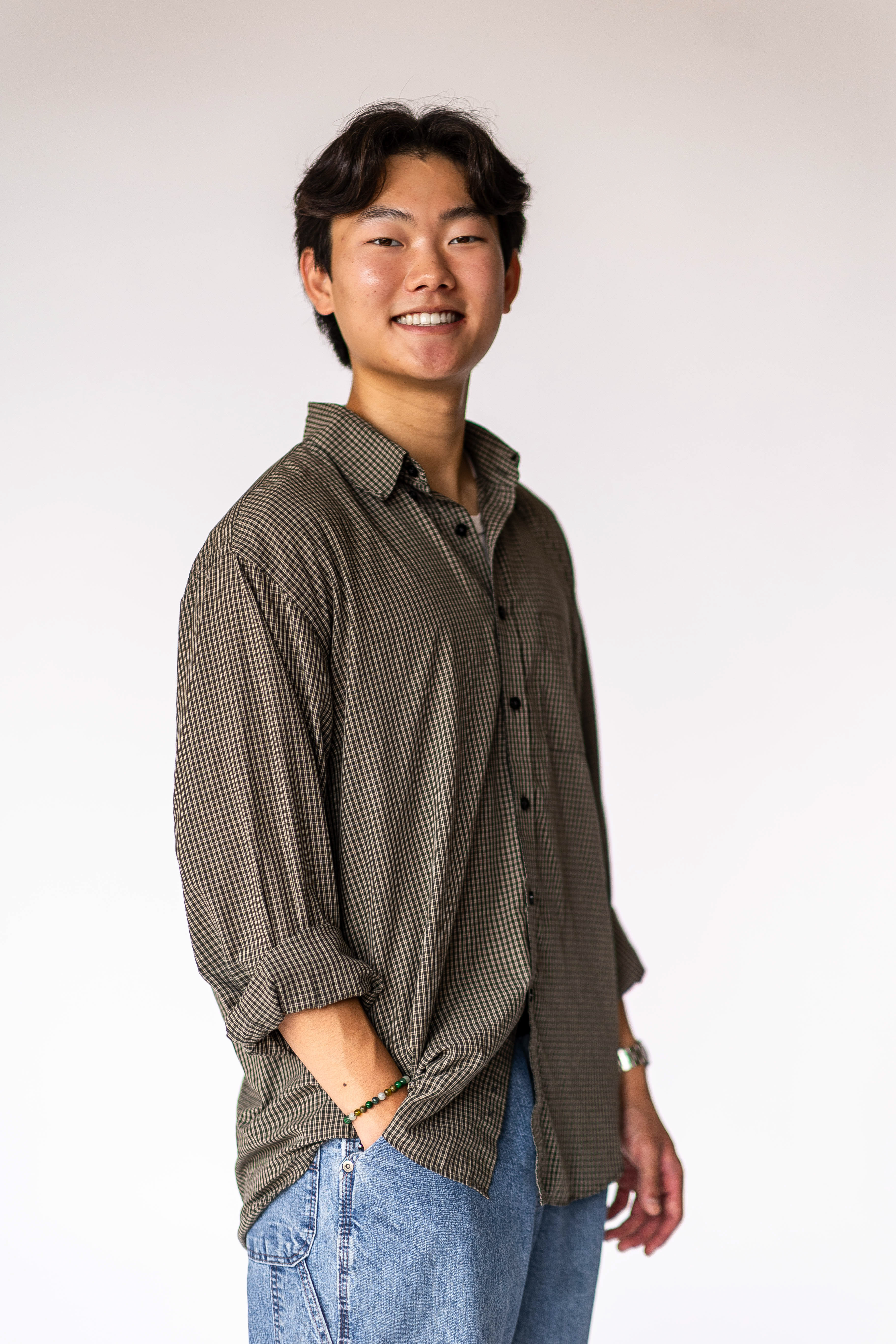 Student wearing button down shirt stands smiling with hand in pocket