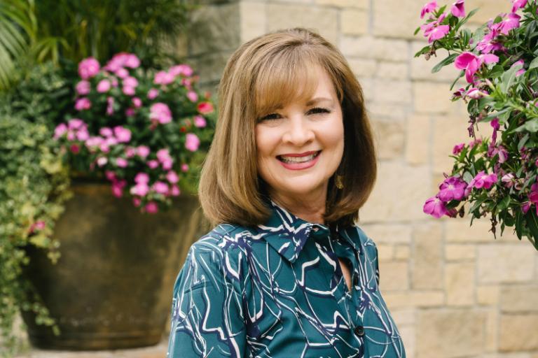 Woman in blue dress standing on steps in front of pink flowers