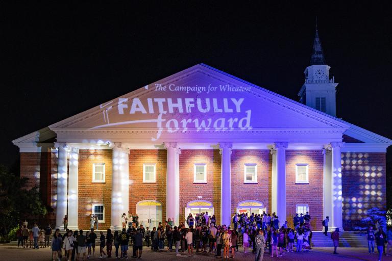 Edman Chapel illuminated by Wheaton blue and orange and Faithfully Forward logo