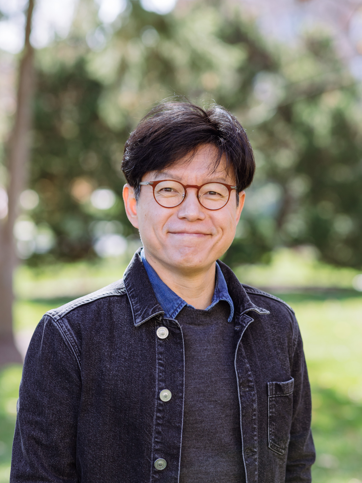 An East Asian man wearing glasses smiles
