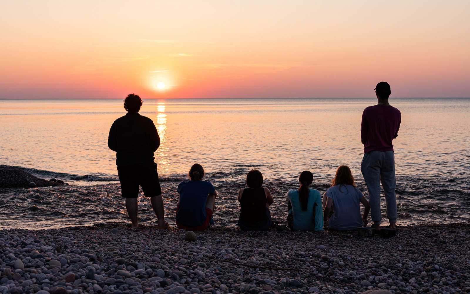 Six young adults on a beach look at a sunset
