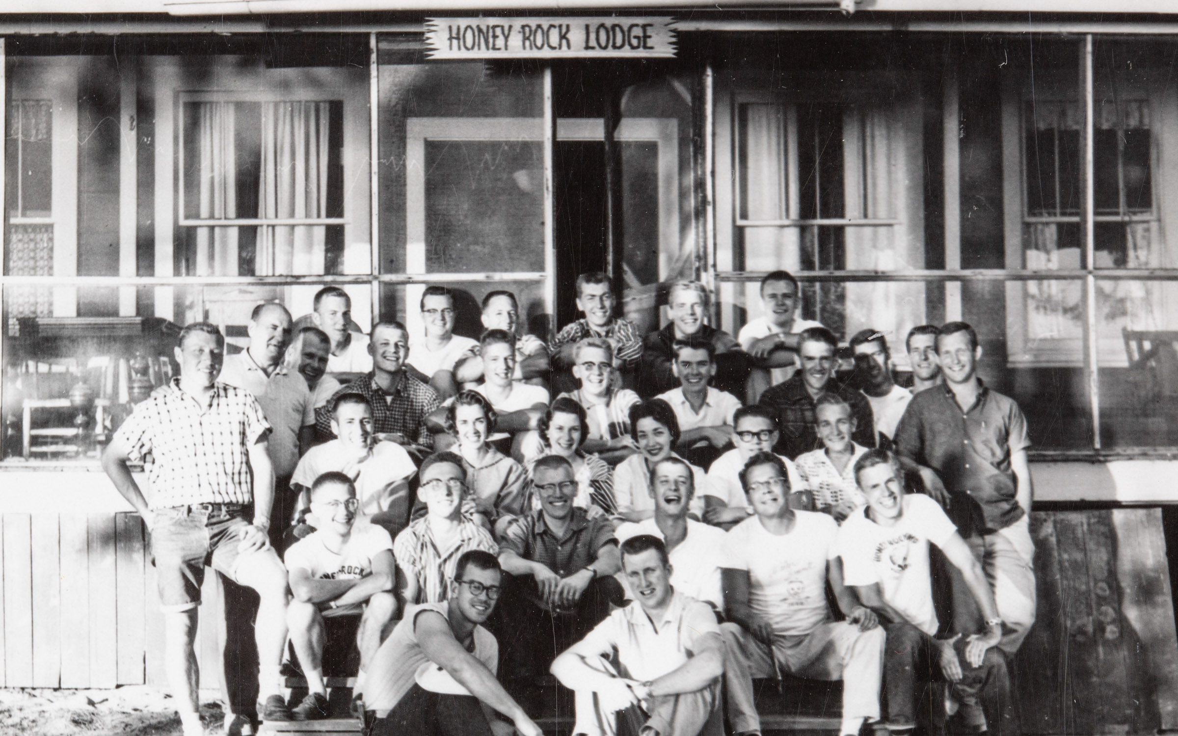 A black and white photo of a group of men and women in front of a building labeled Honey Rock Lodge