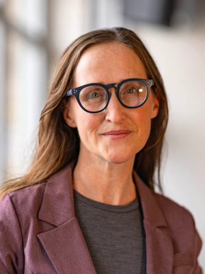 A woman with light brown hair and glasses smiles